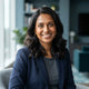 A smiling South Asian parent posing for an authentic, professional portrait against a muted blue and teal background.